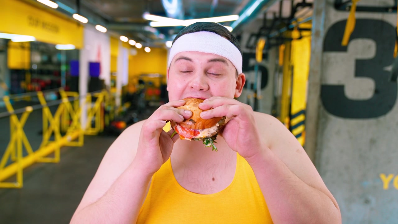 Uomo in sovrappeso che si concede un hamburger in palestra