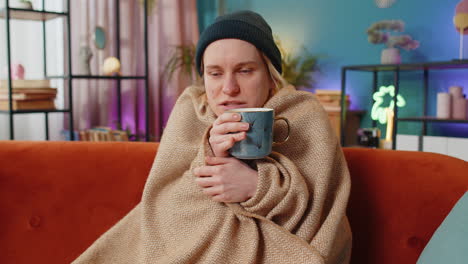 ill sick unhealthy woman freezes from the cold feels bad covered by warm blanket drinks tea at home