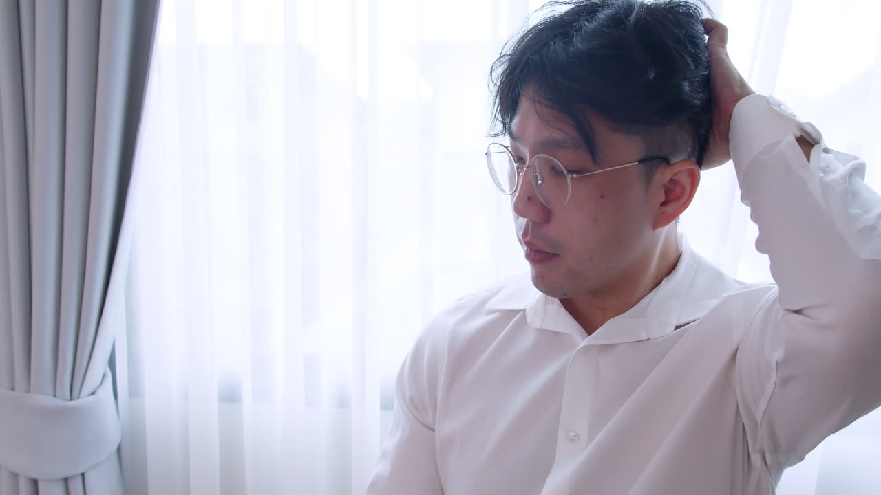 안경을 쓰고 건강한 머리를 하고 카메라를 바라보며 머리를 정리하여 자신을 망치는 아시아 남자를 닫습니다