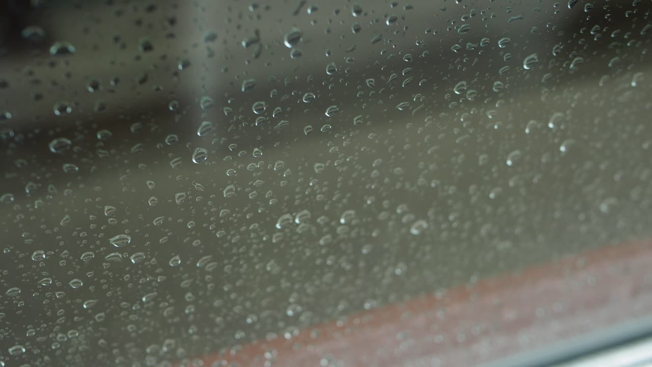 A close-up view of raindrops running down a window, capturing the moody and serene atmosphere of a rainy day.