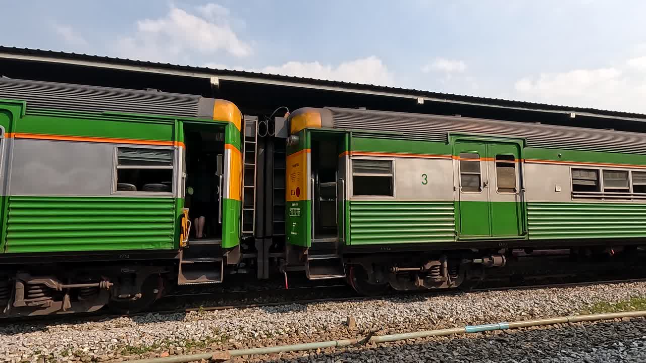 Side view of classic green passenger train slowly departing sunny Bangkok rail platform, handheld shot