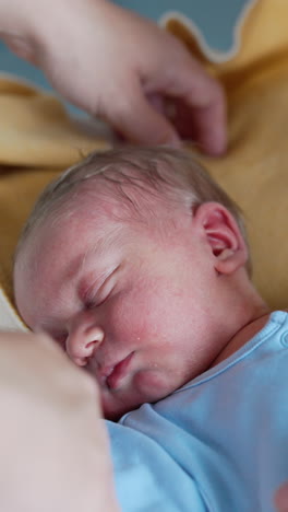 loving parents stand near their sleeping newborn. tiny baby boy in blue romper resting caressed by dad's hand. close up. vertical video