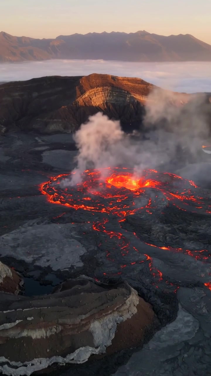 Vertical video: Pulsing lava pond spawning channels as crust cracking and steam rising at dawn