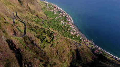 Aerial-tilt-up-shot-looking-down-from-mountains-at-town-by-ocean-coast-in-Madeira