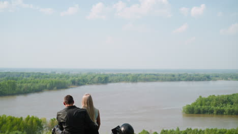 lovely couple sits resting on motorcycle on green hill