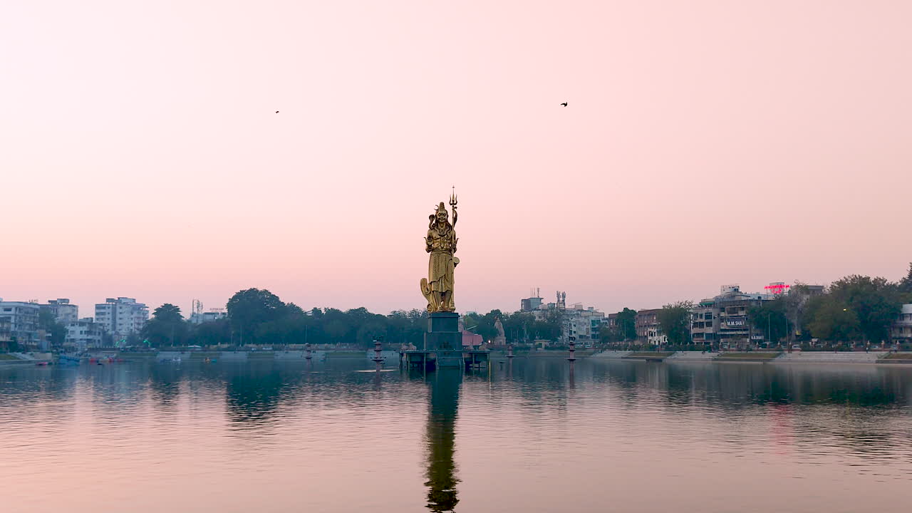maravillarse de la majestuosa vista frontal de la inmensa estatua dorada del señor shiva en el lago sursagar, vadodara, a medida que se pone el anochecer, ofreciendo un espectáculo impresionante de grandeza divina