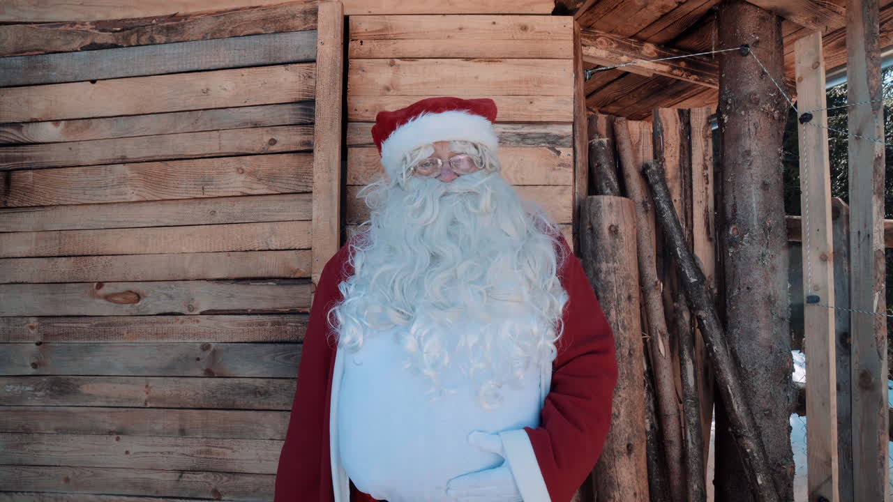 santa habla frente a una pequeña casa de madera en invierno