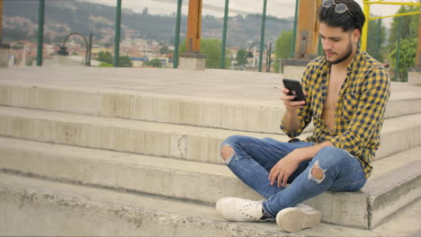 Handsome-guy-sitting-on-stairs-working-on-his-laptop-and-cellphone