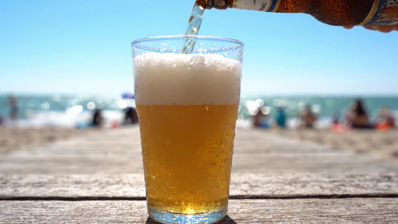 Birra rinfrescante versata in un bicchiere in spiaggia, circondata dalla luce del sole e dal relax, ideale per una perfetta giornata estiva in riva al mare.