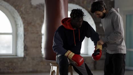 assistant helping to put on boxing gloves to a male athlete