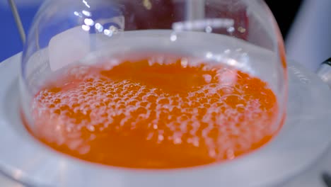 laboratory round bottom flask heating equipment - boiling orange liquid: closeup