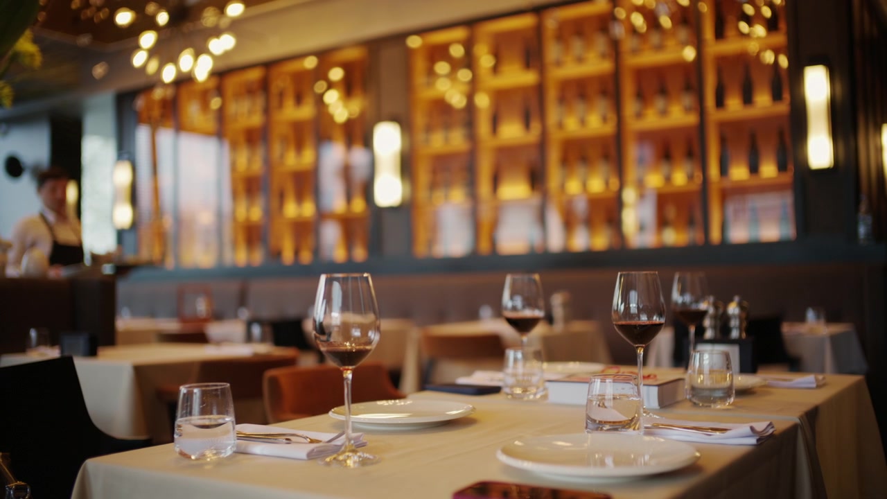 Allestimento elegante di un tavolo da ristorante con numerosi calici da vino, piatti e un'illuminazione ambientale calda.
