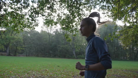 Captivating-slow-motion-shot-of-a-woman-running-from-the-side-in-a-green-environment-with-trees,-as-the-camera-smoothly-follows-her