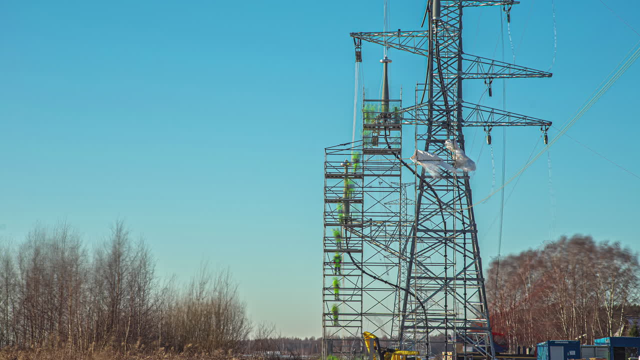 linieros ejecutando líneas en una torre de línea eléctrica recién erigida con la ayuda de una grúa - lapso de tiempo