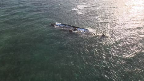 drone aerial moving slowly over waves crashing into a shipwreck during sunset