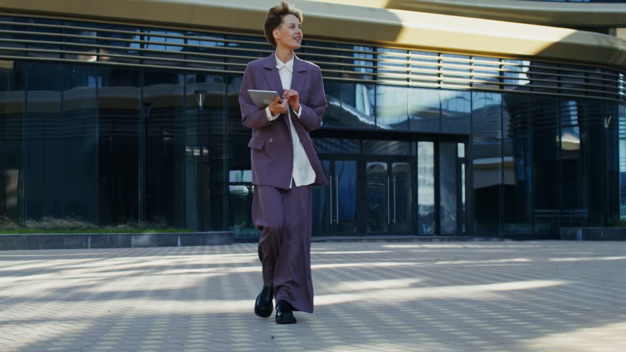 Businesswoman Walking with Tablet in Front of Modern Building