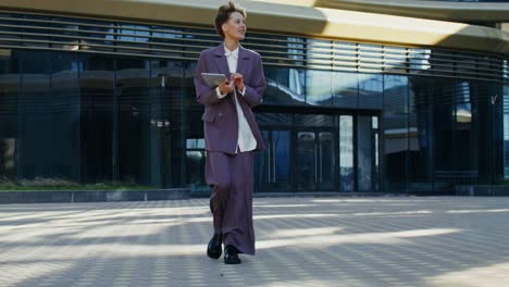 mujer de negocios caminando con una tableta frente a un edificio moderno