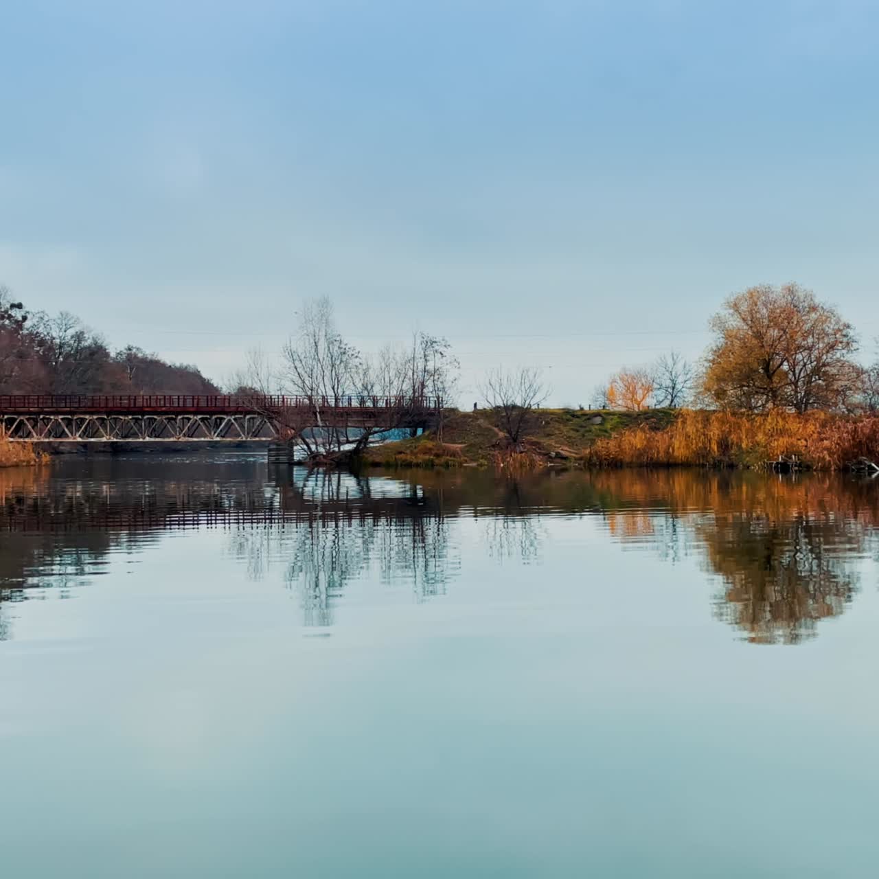River banks joined by the metal bridge. Clear autumn day in the nature that started to fade. Dry grass growing on the waterfront