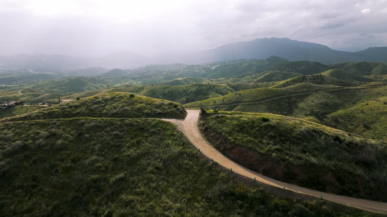 Drone video of a dirt road winding through a mountainous landscape near Marbella, Spain, with lush natural surroundings.