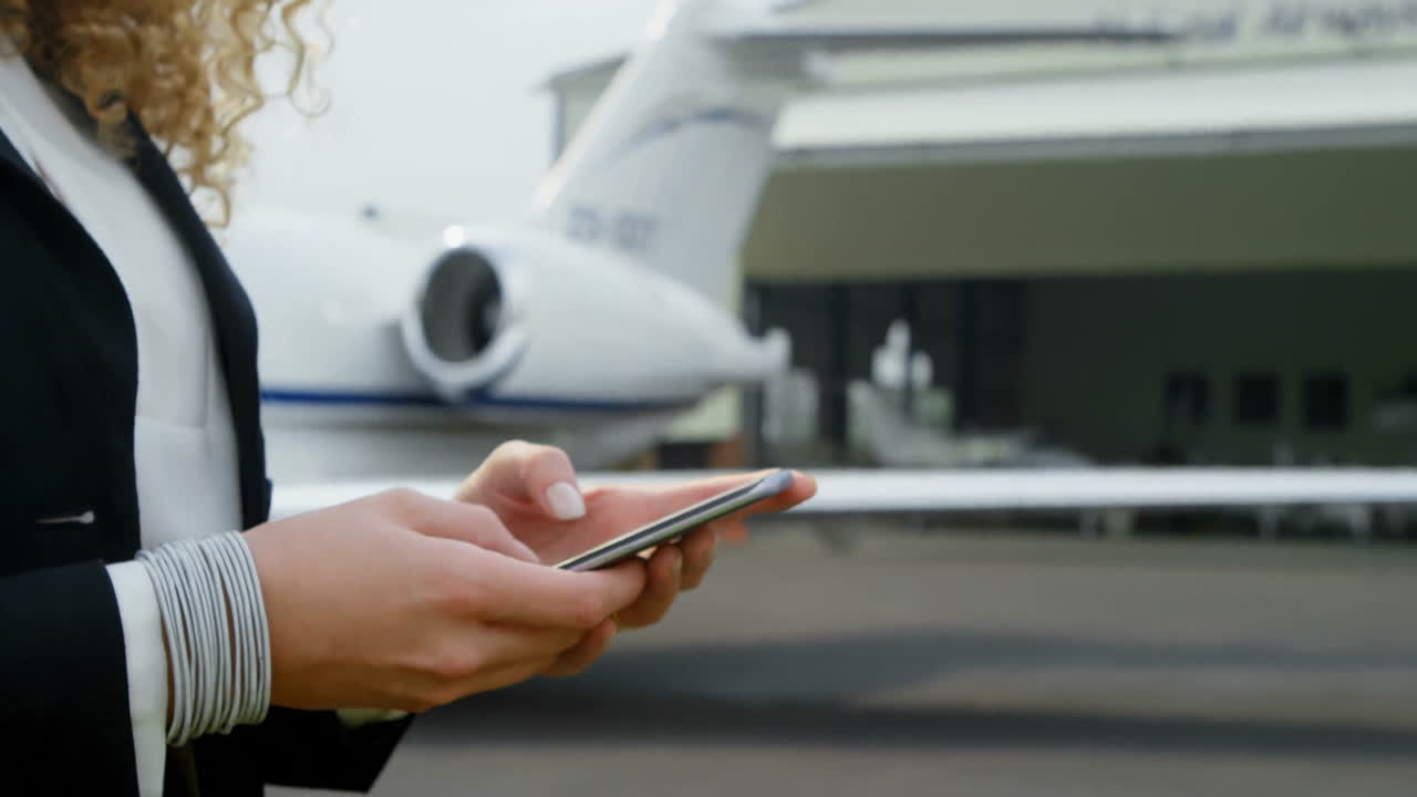 Using smartphone, person standing near private jet at airport runway