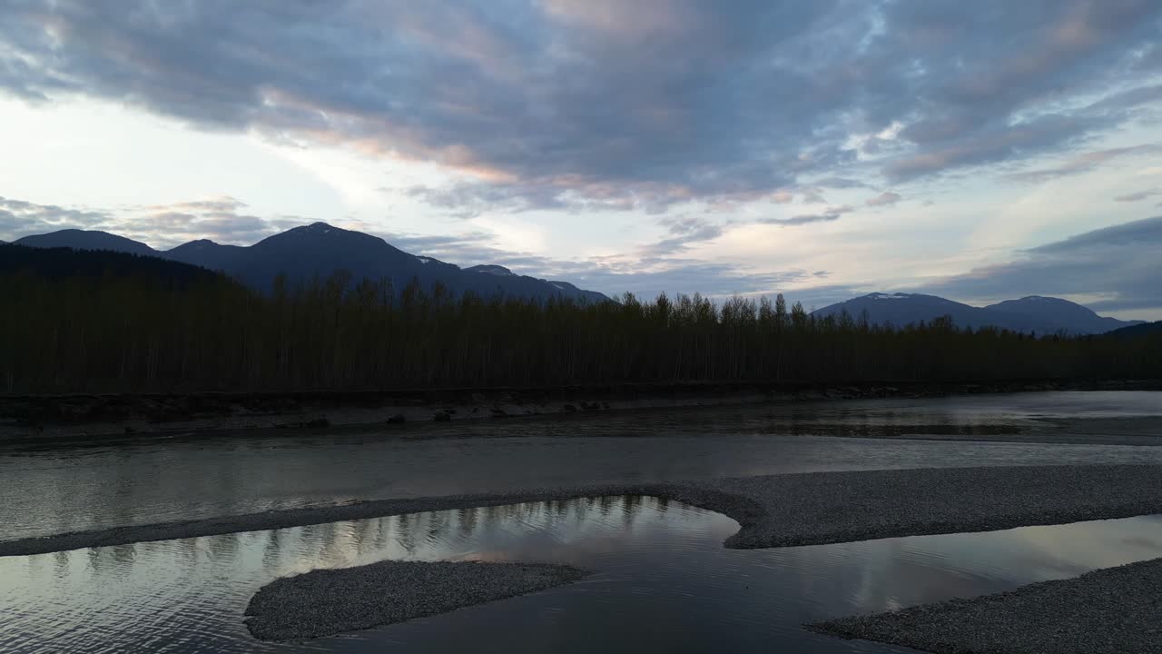 río, orilla con árboles y montañas al atardecer