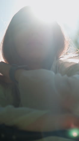 반투명한 레인코트를 입은 여자의 클로즈업, 후드를 내려놓고 빛으로 그녀의 사려 깊은 표정을 강조하며, 그녀는 잔잔한 초록색이 백그라운드에서 부드럽게 흐릿하게 손을 고 있습니다.