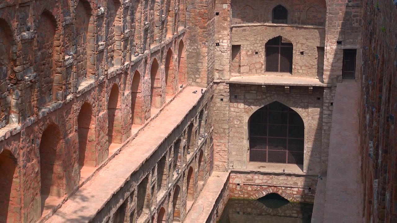 Nedadgående panorering langs gamle røde sandstensbuer for at afsløre vandbassinet ved Agrasen Ki Baoli trinbrønden i New Delhi, Indien