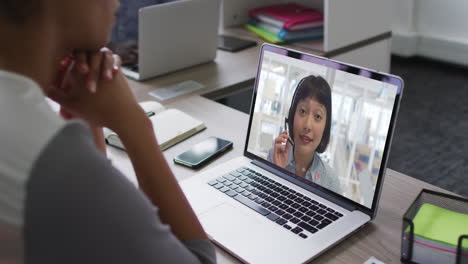 Mid-section-of-african-american-woman-having-a-video-call-on-laptop-with-female-colleague-at-office