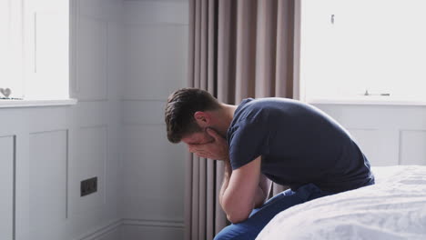 man wearing pajamas suffering with depression sitting on bed at home