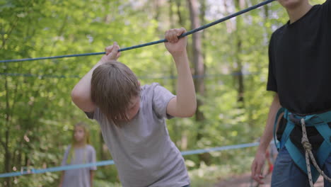 children on a summer camp hike are moving along the ropes with the help of a guide who teaches children rock climbing and tourism. a boy in the forest overcomes a rope barrier