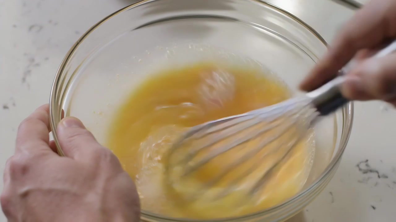 Whisking cook hands as whisk entering glass bowl on kitchen counter, combining eggs for breakfast