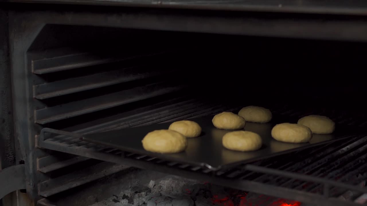 Bakerkokk la hamburgerboller av deig inn i en kullfyrt ovn for brødtilberedning på en gourmetrestaurant