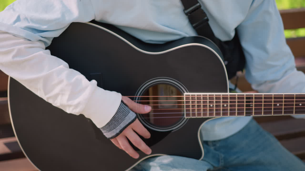 Muzyk grający na gitarze. Swobodny artysta z gitarą akustyczną. Niezależny artysta cieszący się spokojną sesją gry na gitarze na świeżym powietrzu. Jasne naturalne otoczenie z muzykiem brzdąkającym na gitarze akustycznej na drewnianej ławce.