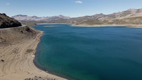 Panning-aerial-view-of-the-maule-lagoon-at-the-pehuenche-border-crossing-between-chile-and-argentina-on-a-sunny-day-with-the-andes-mountains-in-the-background