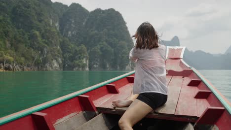 woman on a longtail boat enjoying the scenic view of a lake surrounded by mountains in thailand
