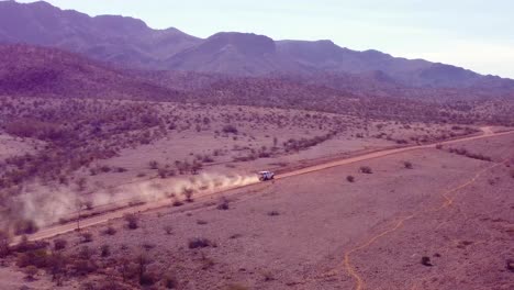 a white car kicks up dust as it speeds along a remote dirt road, leaving a trail of dust in its wake