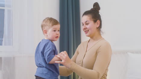 happy young woman cuddling and kissing her cute baby boy while playing together on the bed at home