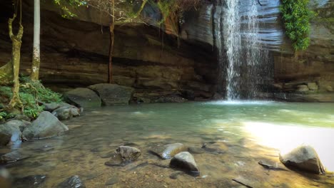 Secluded-lagoon-and-waterfall-flow-over-cave-shelter-in-a-tropical-location