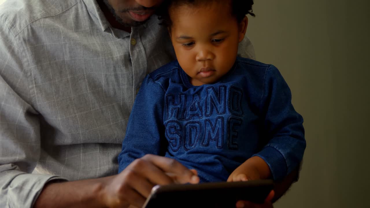 Front view of black father and son using digital in a comfortable home 4k