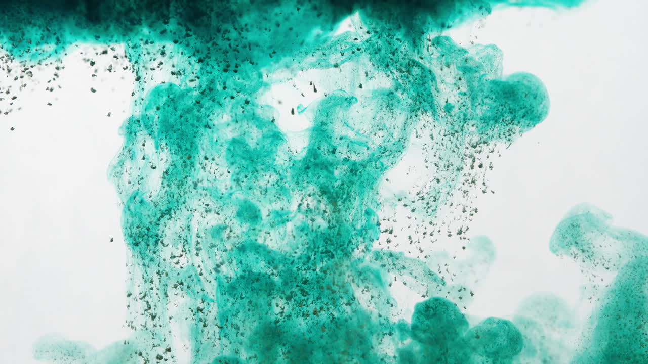partículas verdes oscuras que se ven fluyendo y disolviéndose en agua clara