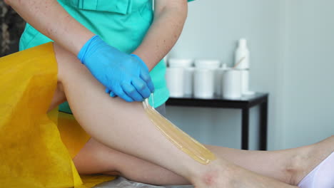 The-girl-talks-on-the-phone-and-smiles-during-hair-removal-on-the-legs-in-the-beauty-salon.-Hair-removal-on-the-legs-with-sugar.-clouse-up