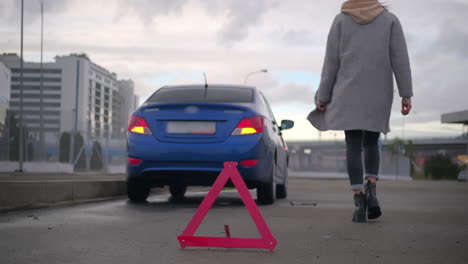 woman walking away from broken-down car on the side of the road