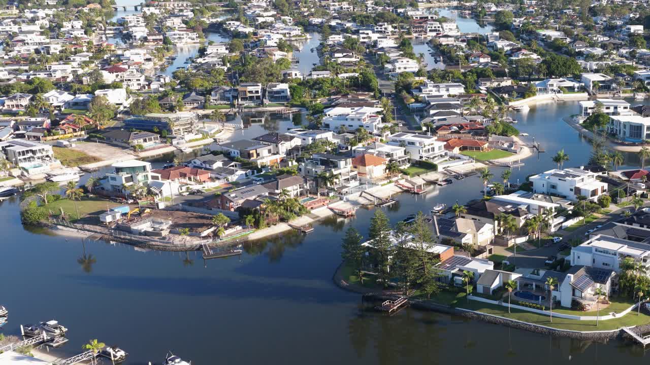 Aerial footage captures the serene residential canals of Gold Coast, Australia, under bright daylight, showcasing modern architecture and lush greenery