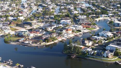 aerial footage captures the serene residential canals of gold coast, australia, under bright daylight, showcasing modern architecture and lush greenery