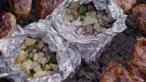 stirring grilled zucchini with metal tongs on a charcoal black kettle grill at a public park in summer