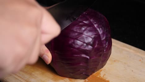 mano caucásica corta una col roja en dos con fuerza en la tabla de cortar de madera