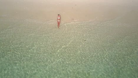 aerial view of young caucasian woman in bikini on white sandy beach in asia - camera tracking backwards