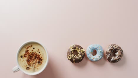 Video-of-donuts-with-icing-and-cup-of-coffee-on-pink-background