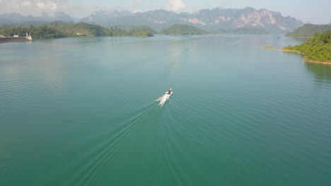 motorboat sailing in colorful lagoon of exotic island, tilt up aerial. turquoise water and green coast of krabi island, thailand