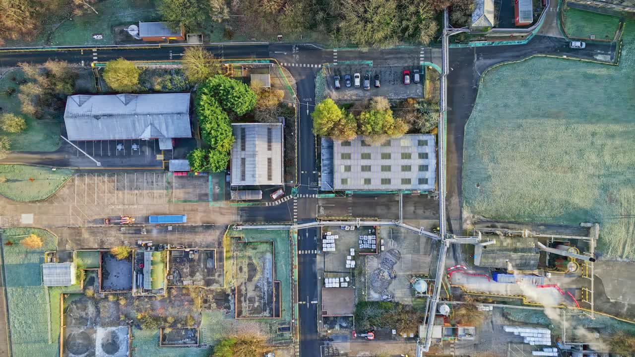 배관 구조, 건물, 냉각탑, 증기 및 작업 차량을 보여주는 대형 산업 플랜트의 오버헤드 항공 영상